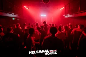 foto van een zaal met veel rood licht en een led bord waar helemaal house op staat